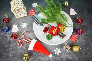 Christmas table place setting decoration with gift box ball candy cane in santa claus hat fork and knife plate Xmas New Year food lunch festive Christmas dinner holidays background themed party photo