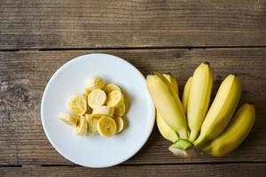 Cáscara de plátano en rodajas sobre un plato blanco y fondo de madera, plátano pelado listo para comer. foto