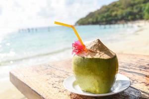 Coconut tropical fruit on table and sand beach background water - Fresh coconut juice summer with flower on beach sea in hot weather ocean landscape nature outdoor vacation , young coconut photo