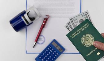 la mano sostiene el pasaporte de uzbekistán con dólares estadounidenses en el fondo de los documentos y el sello de goma. concepto - soborno y corrupción