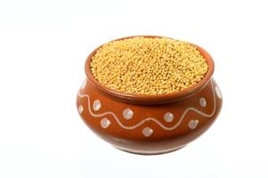 yellow mustard seeds in clay pot isolated on white background photo