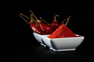 chilly powder with red chilly in white plate, dried chillies on black background photo