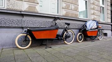 dusseldorf, alemania - 20 de febrero de 2020. una bicicleta para mamá y bebé con cuna y asiento infantil para transportar niños está protegida del viento. vida en europa. caminando con niños. foto