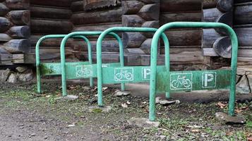 El estacionamiento de bicicletas de metal está pintado de verde sin bicicleta, en el campo cerca de una casa de madera. Espacio de almacenamiento para vehículos de dos ruedas. foto