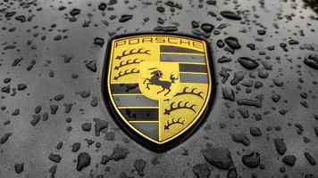 Ukraine, Kiev - March 27, 2020. Porsche logo close up on a black car with raindrops. Hood emblem of a sports car. copy space, editorial photography. German car exhibition on the street.