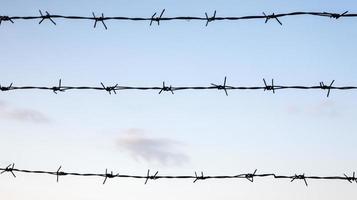 Barbed wire against a blue sky closeup. Fence or fencing in a closed area. photo