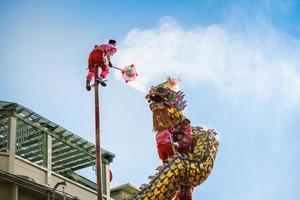 Nakhonsawan Thailand-Feb 4, 2022. Performance of dragon dance on pole. Dragon mule crystal ball. Man standing on wooden pole holding replica of crystal ball stave. Dragon spews holy water. photo