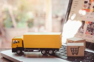 logística y servicio de entrega: camiones y cajas de papel o paquetes con el logotipo de un carrito de la compra en un teclado portátil. servicio de compra en la web online y ofrece servicio a domicilio. foto
