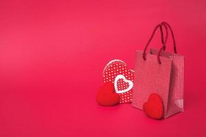 On a red background, a gift bag with a heart shaped box. The concept of valentines day, mothers day, sale. With copy space, closeup photo