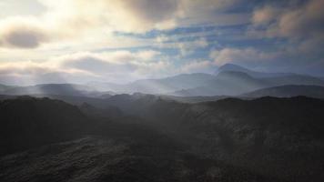 schwarzer Vulkanstaub und Berge mit Nebel im Hintergrund