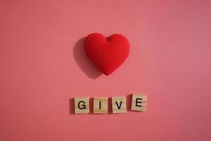 Red heart with letter words of Give isolated on pink background. Giving, sharing, charities and donate concept. photo