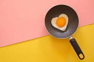 Heart shape fried egg in the pan on yellow and pink background. top view. healthy food  concept.  Copy space for text photo