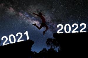 mujer deportiva salta sobre la montaña en el fondo de la vía láctea del cielo nocturno. salto femenino 2021 a 2022 concepto de feliz año nuevo.