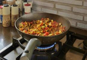 Dish with eggplant, zucchini and bell pepper is fried in pan on gas stove photo