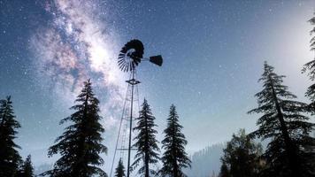 molino de viento retro en bosque de montaña con estrellas. hiperlapso foto