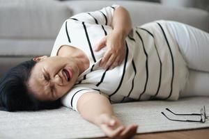 primer plano de una mujer asiática que sufre un ataque al corazón tirada en el suelo sola en casa. mujer tocando el pecho y teniendo dolor en el pecho. concepto médico y de salud. foto