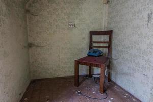 silla de madera y un teléfono en la esquina de una habitación con telarañas foto
