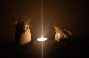 two figures made of stone looking to a burning candle in the dark photo