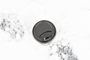 A large disposable paper cup with a lid for hot drinks on a snowy background. photo