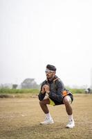 Young Indian sports man doing squats in the field. Sports and healthy lifestyle concept. photo