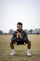 foto frontal de un niño indio haciendo sentadillas en el campo con ropa deportiva. concepto de deportes y estilo de vida.