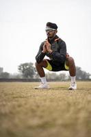 Young Indian sports man doing squats in the field. Sports and healthy lifestyle concept. photo