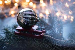 composición navideña con trineo pequeño y bola de navidad en el árbol de navidad. fondo bokeh. foto