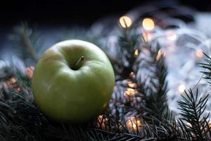 manzana verde en la rama del árbol de navidad. fondo bokeh con guirnalda. el concepto de alimentación saludable durante las vacaciones de año nuevo foto