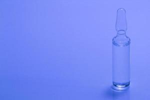 Medical ampoule on a blue background. Glass ampoule for injection with medicine on the table. Concept medicines and disease treatment. Pharmacology, cosmetology, science. Copy space for text. Close-up