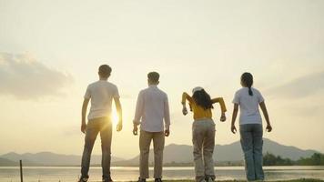 vier mensen groep gelukkige tieners die handen opsteken die op zonsondergangberg en rivierachtergrond springen. video