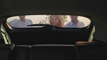 drei leute junge asiatische männer und frauen, die gepäck aus dem kofferraum eines autos lebensstil urlaub reise roadtrip tragen.