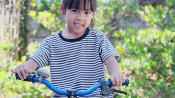 alegre niña sonriente tocando una campana de bicicleta en un manillar de bicicleta, preparándose para andar en bicicleta en un parque. video