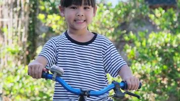 alegre niña sonriente tocando una campana de bicicleta en un manillar de bicicleta, preparándose para andar en bicicleta en un parque. video