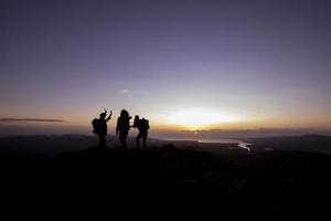 tres siluetas de personas al amanecer en la cima de una montaña foto