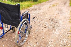 Empty wheelchair standing on road waiting for patient services. Wheel chair for people person with disability parked outdoor. Accessible for person with disability. Health care medical concept. photo