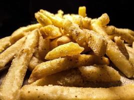 Close up photo of french fries on a wooden cutting board, with black background.