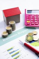 Coin stack with red house and calculator and pen on business report backgrounds vertical photo