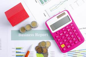 Pink calculator and money coin with red house on business report backgrounds above photo