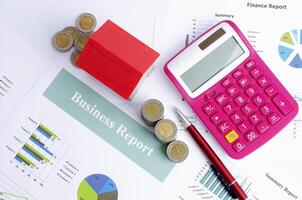 Red house and money coins and pen and calculator on business report paper backgrounds above, Top views photo