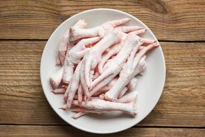 patas de pollo en plato blanco, patas de pollo crudas frescas para comida cocinada en el fondo de la cocina de mesa de madera, vista superior foto