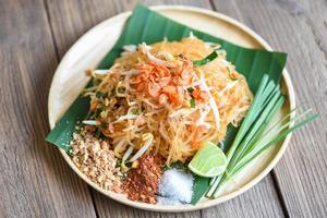 Fideos salteados pad thai en un plato servido en la mesa del comedor comida, comida tailandesa fideos fritos al estilo tailandés con gambas brotes de soja y guarnición de cacahuetes chile en polvo azúcar limón lima - vista superior foto