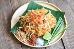 Stir-fry noodle Pad Thai on plate served on the dining table food, Thai food fried noodle Thai style with prawns bean sprout and garnish peanuts chili powder sugar lemon lime - top view photo