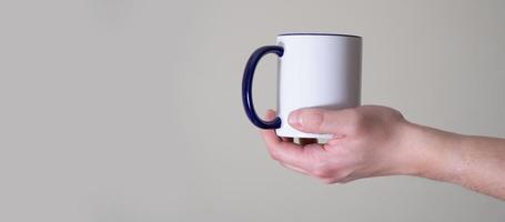 White mug in the hands of a man on a light background. photo