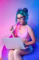 a woman in a bright bathing suit with blue hair is sitting on a chair bag with a laptop photo