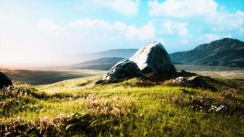 prairie avec d'énormes pierres parmi l'herbe sur la colline au coucher du soleil video