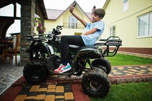 niño en cuatriciclo atv de cuatro ruedas con teléfono móvil. foto