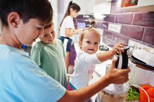 Mother with kids cooking at kitchen, happy children's moments. Work with a blender. photo