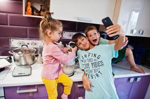 Kids cooking at kitchen, happy children's moments. Making selfie on phone. photo
