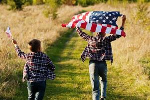 dos hermanos corriendo con la bandera de estados unidos. vacaciones de américa. orgullosos de ser hijos de patria. foto