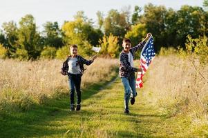 dos hermanos corriendo con la bandera de estados unidos. vacaciones de américa. orgullosos de ser hijos de patria. foto